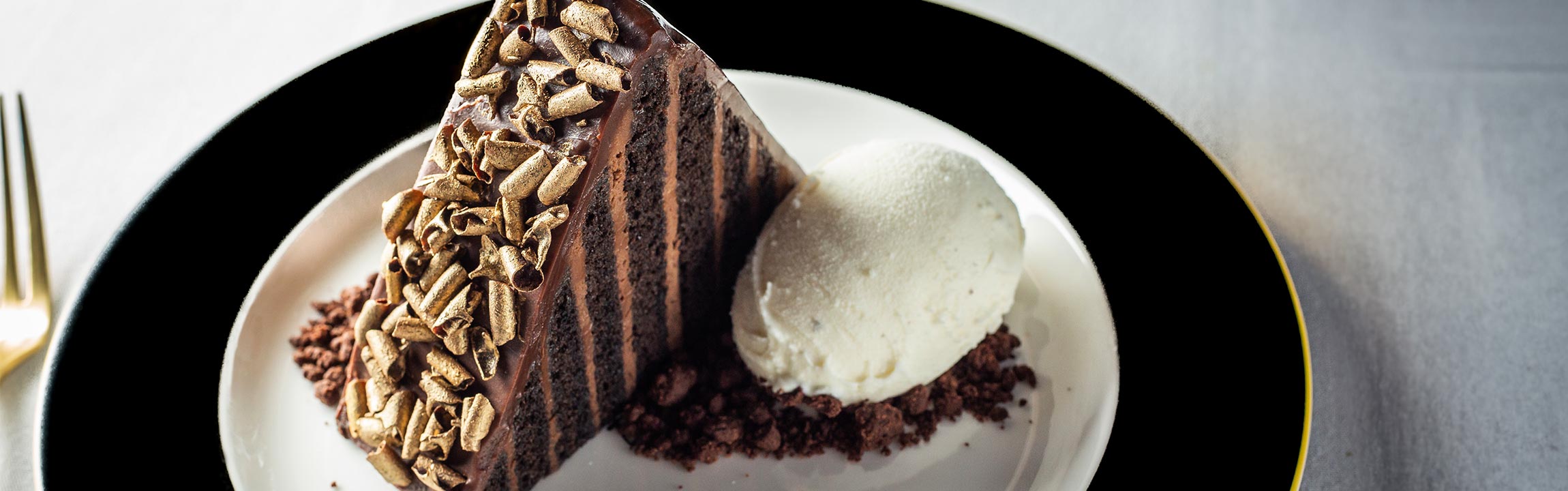 Slice of Chocolate Ganache cake with gold curls and vanilla gelato served at Butcher & Rose in Columbus, Ohio.