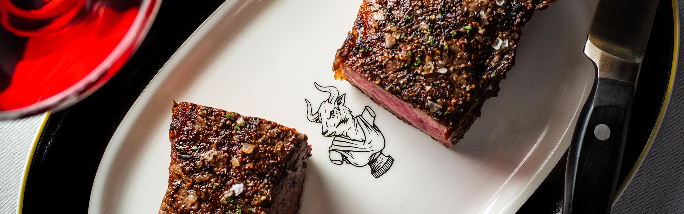 Grilled steak cut in half on presentation plate imprinted with Butcher & Rose minotaur icon.