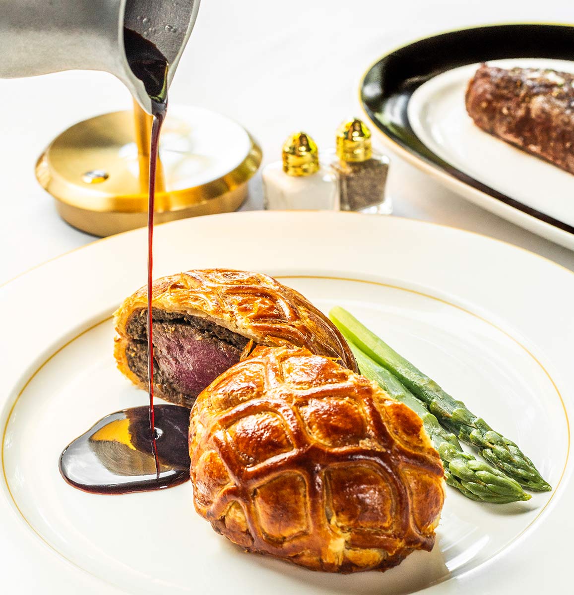 Demi-glace being poured onto plate with Beef Wellington and asparagus spears at Butcher & Rose in Columbus, Ohio.